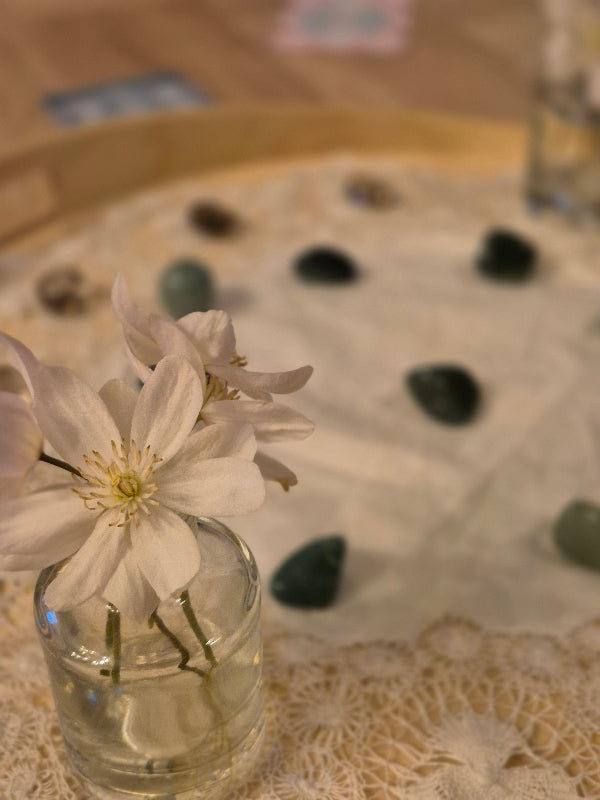 image of a small vase of white clematis flowers in the foreground with green aventurine & smokey quartz laid out behind