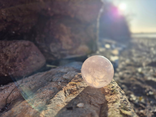 A rose quartz sphere sat on a wall with the sun rising in the background creating a magical reflective orb in the foreground. 