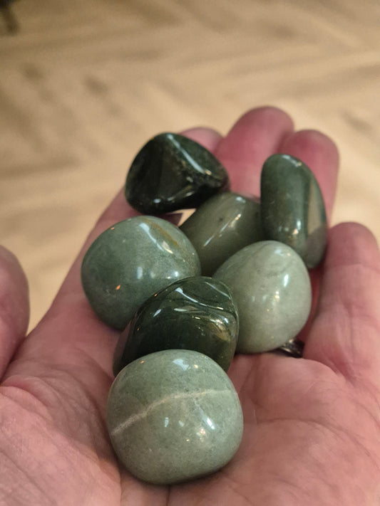 Open hand palm facing upwards filled with green aventurine crystal tumble stones