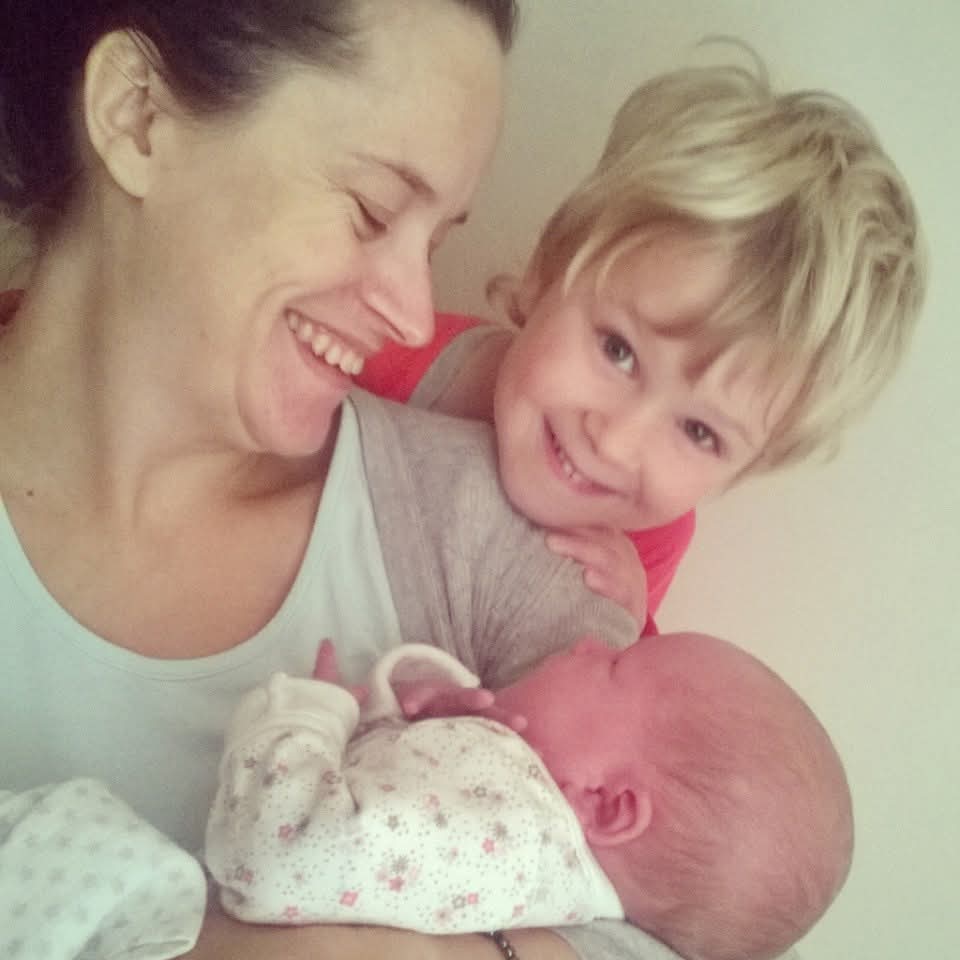 Mama, holding her baby with her little brother chin on shoulder giving a cheeky smile